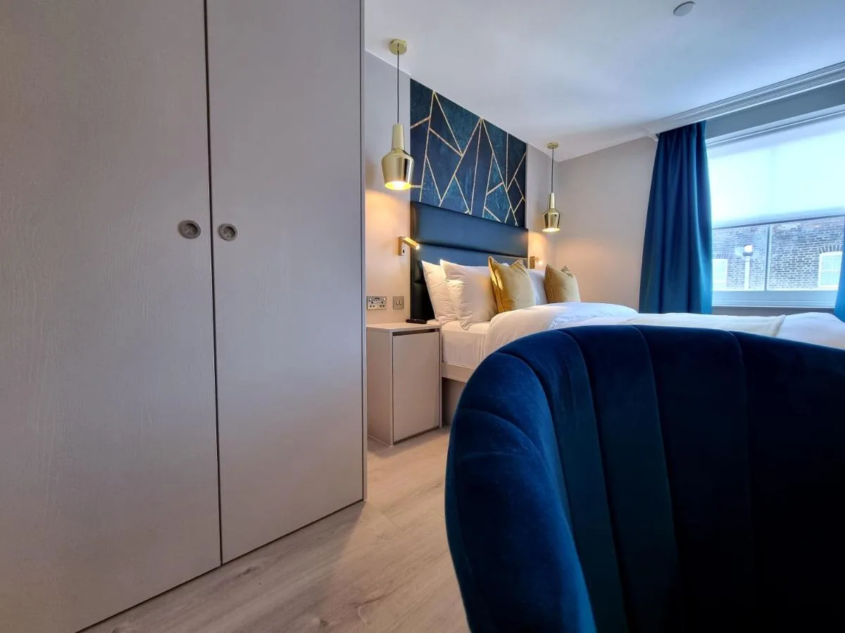 a bedroom with a blue and white bed and a window at NOX Kensington Gardens in London